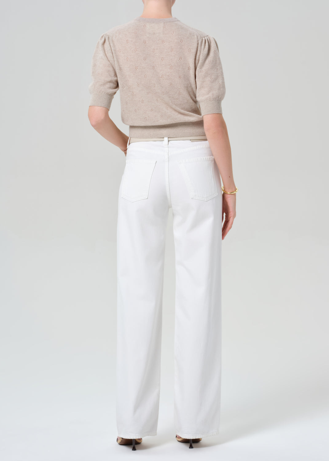 Person wearing a beige cardigan and white jeans on a plain background