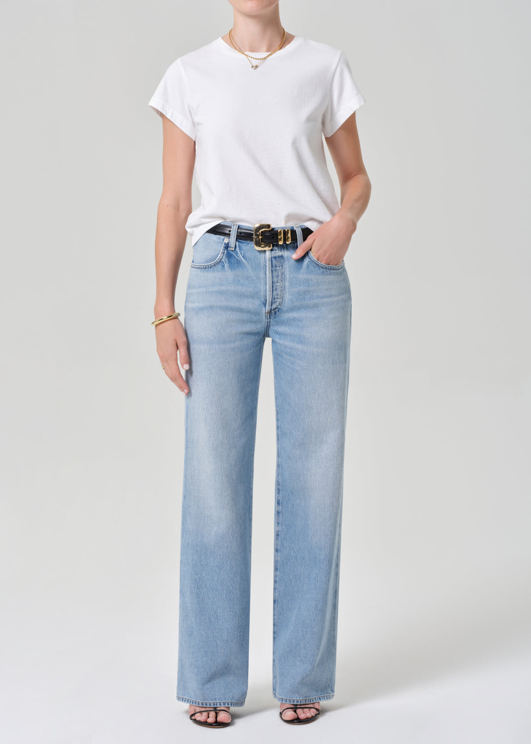 Person wearing a white t-shirt and light blue jeans on a plain background