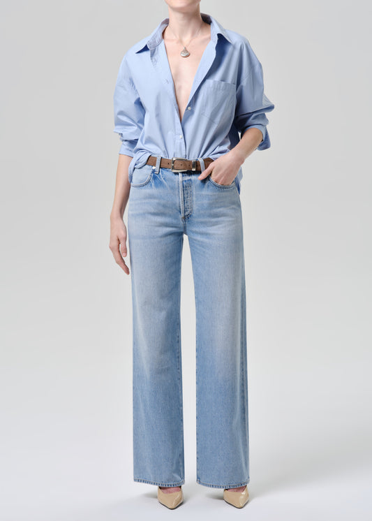 Person wearing a light blue button-up shirt and jeans on a grey background