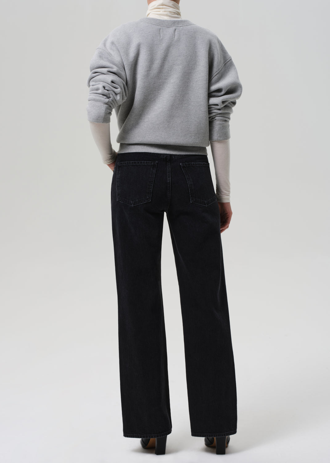 Person wearing a gray sweater and black pants on a white background