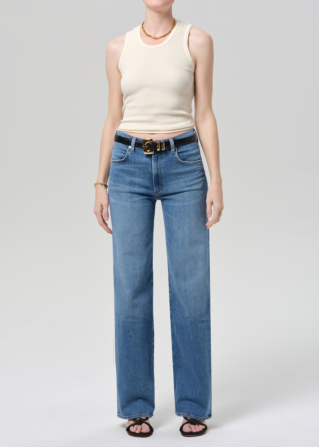 Person wearing a cream sleeveless top and blue jeans on a light gray background