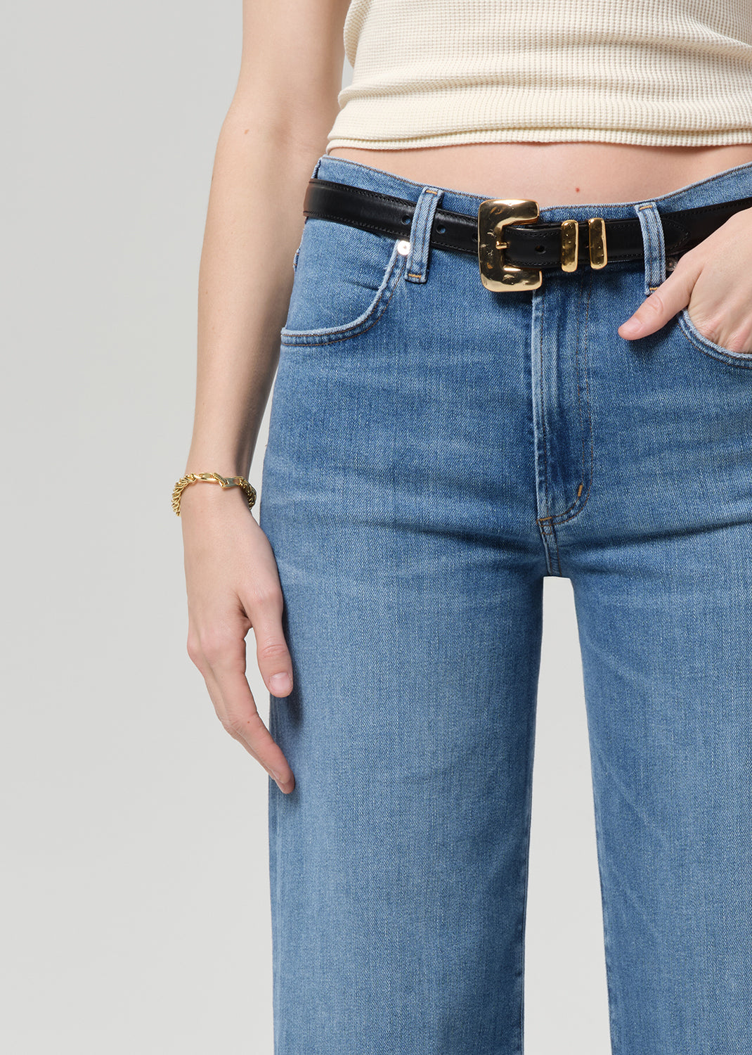 Person wearing blue jeans with a black belt on a plain background