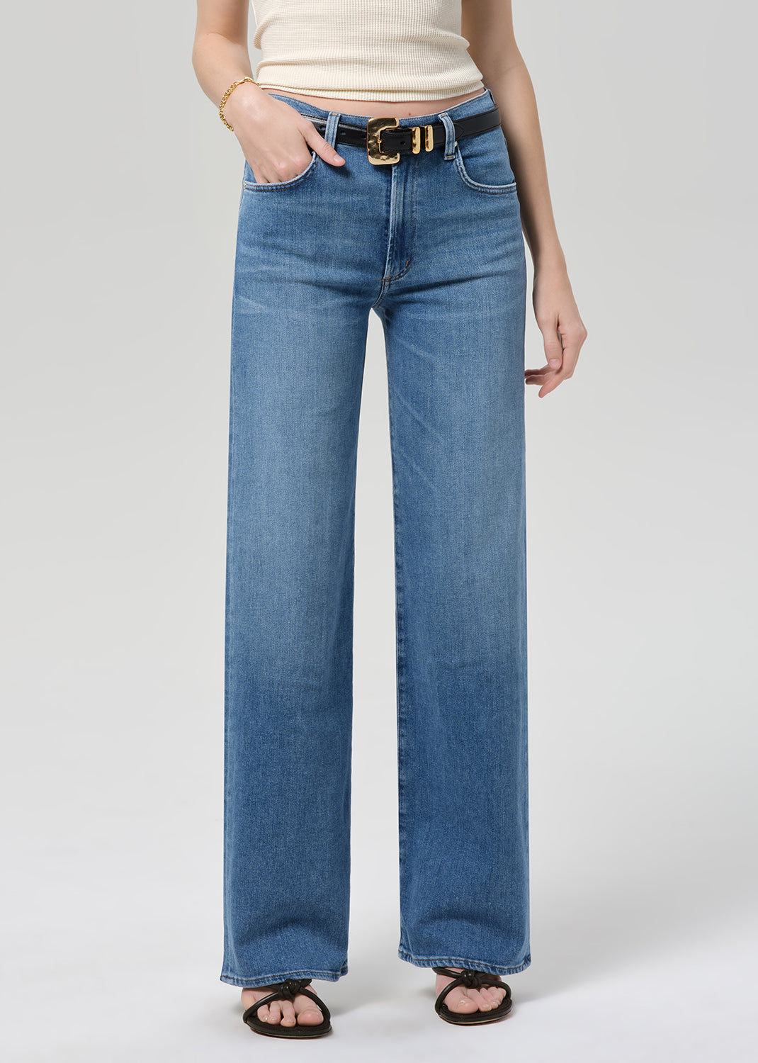 Person wearing blue jeans with a belt on a plain background