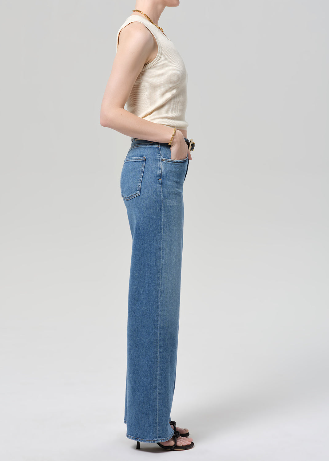 Person wearing a cream sleeveless top and blue jeans on a light gray background