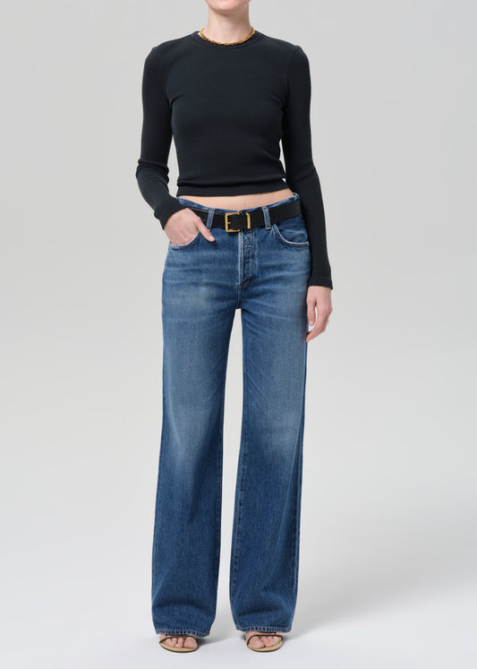 Person wearing a black long-sleeve top and blue jeans on a plain background