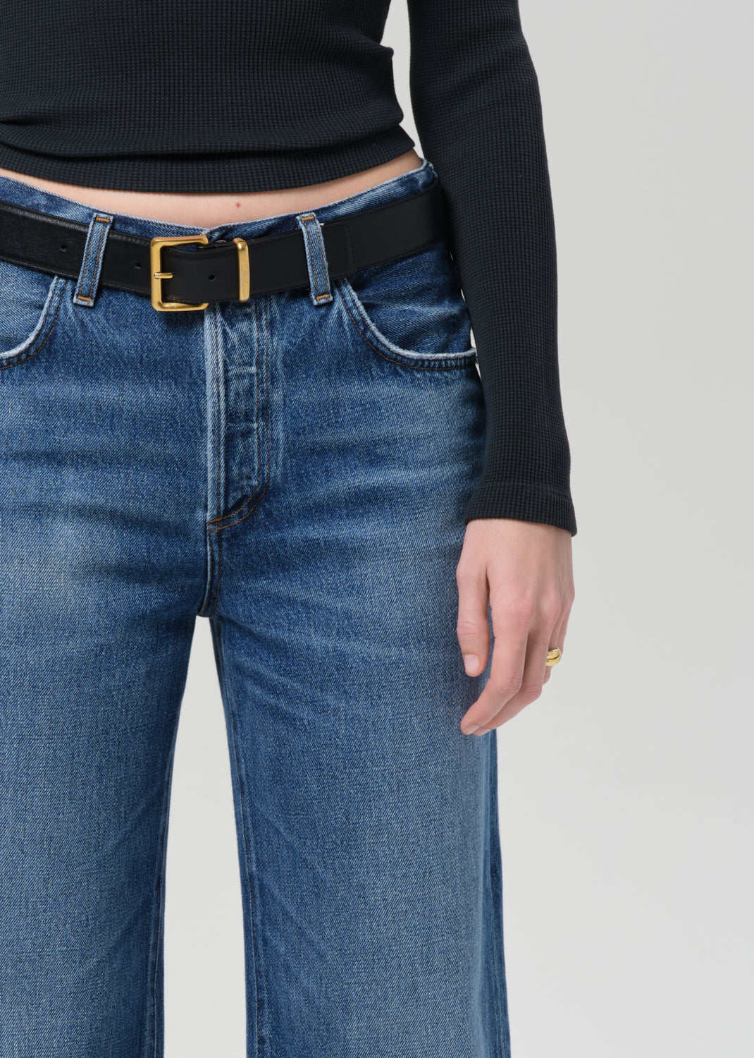 Person wearing a black long-sleeve top and blue jeans on a plain background