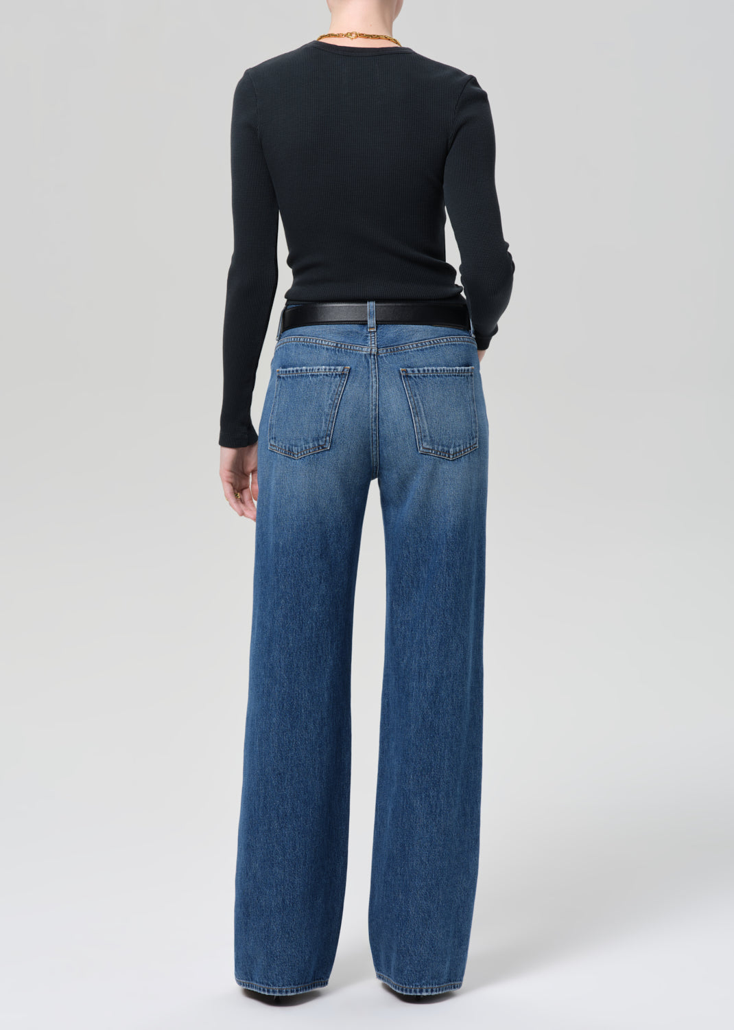 Person wearing a black long-sleeve top and blue jeans on a plain background