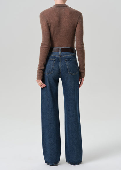 A model shown from the back wearing a brown long-sleeve knit top and high-waisted, wide-leg blue jeans with a dark brown belt, against a grey background.