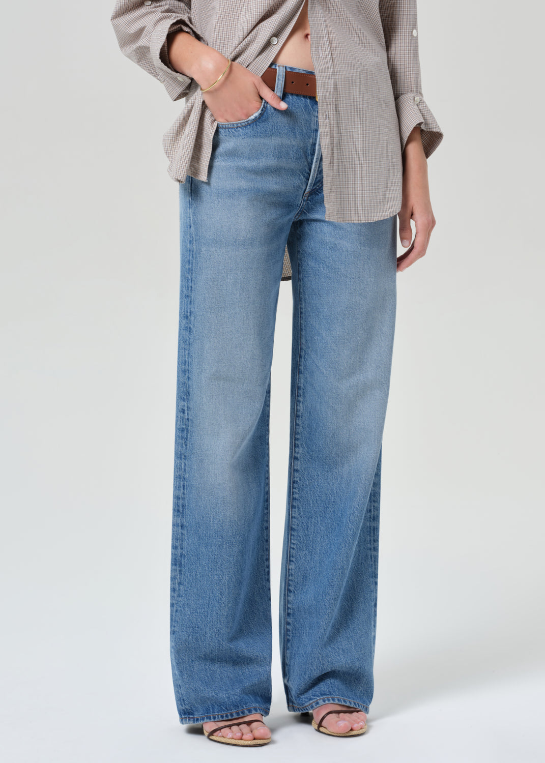 Person wearing a plaid shirt and blue jeans on a grey background