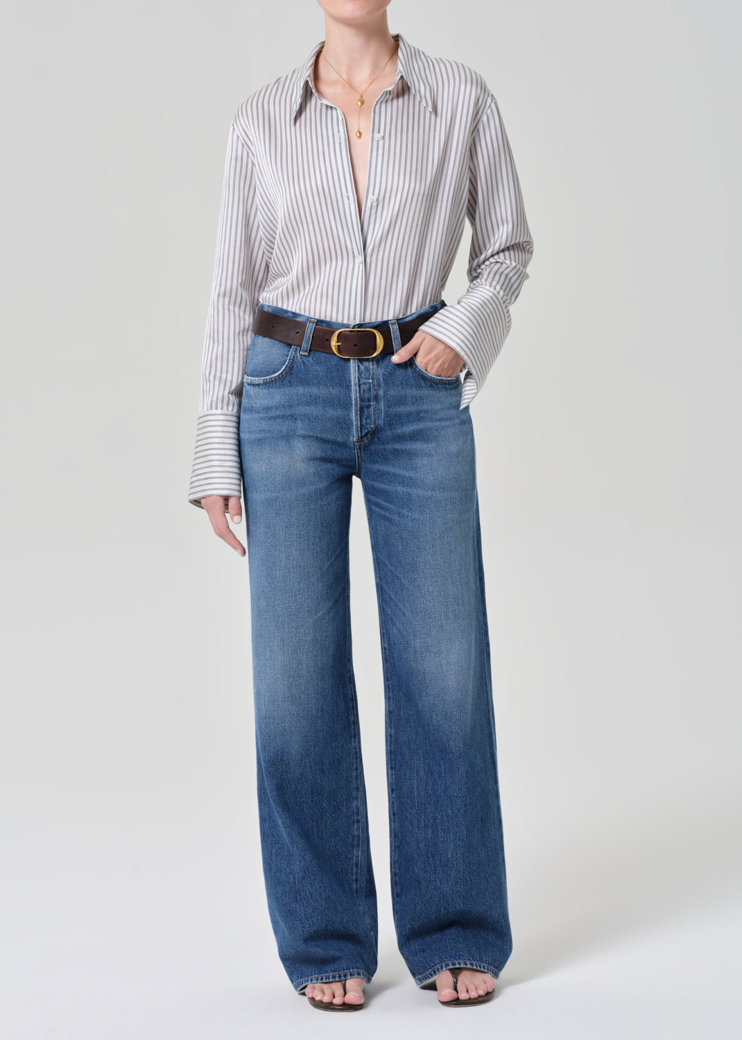 Person wearing a striped shirt and blue jeans on a grey background