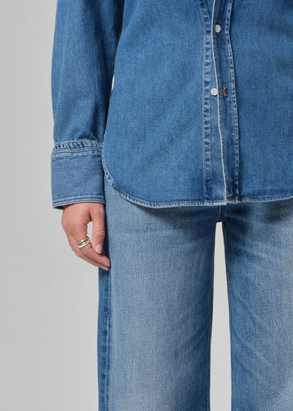 Person wearing a blue denim shirt and jeans on a gray background