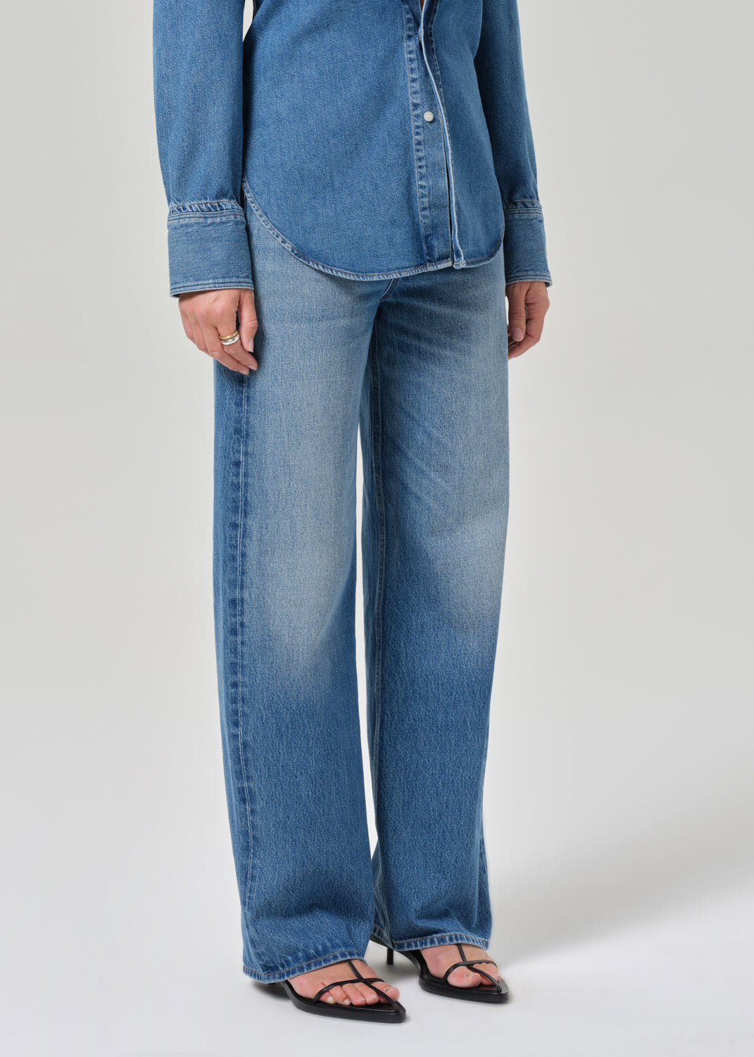 Person wearing a blue denim shirt and jeans on a white background