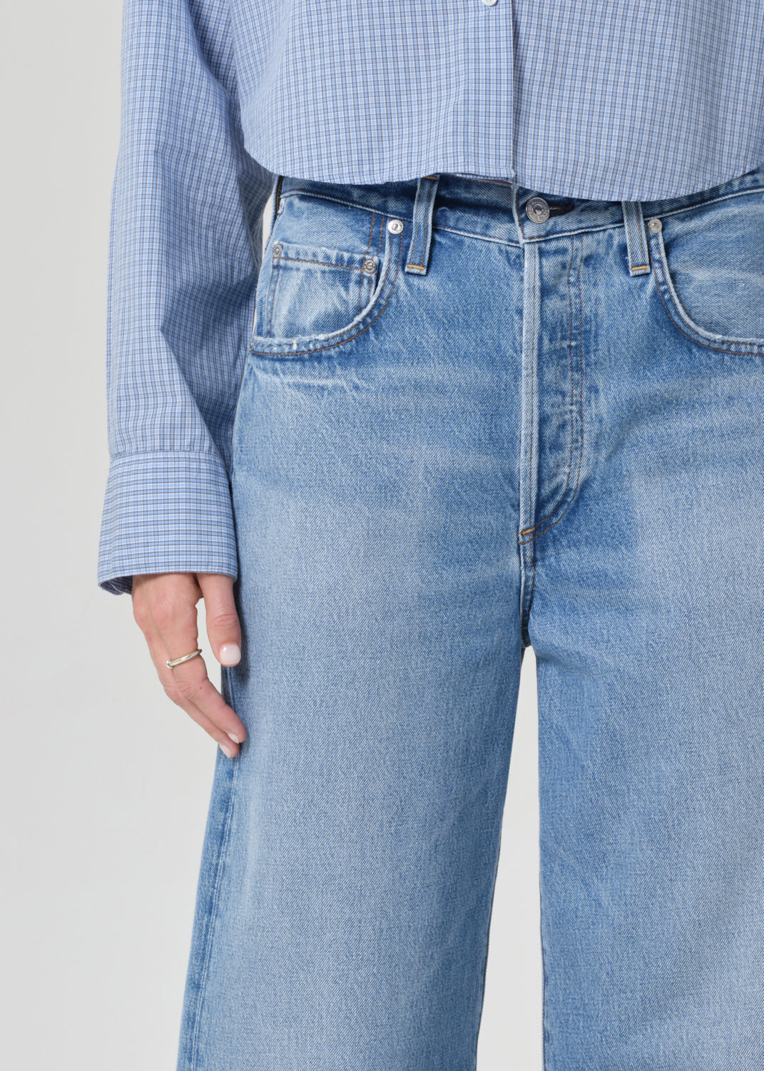 Person wearing a blue plaid shirt and jeans on a grey background