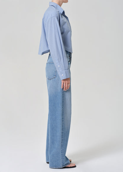 Person wearing a blue plaid shirt and jeans on a grey background