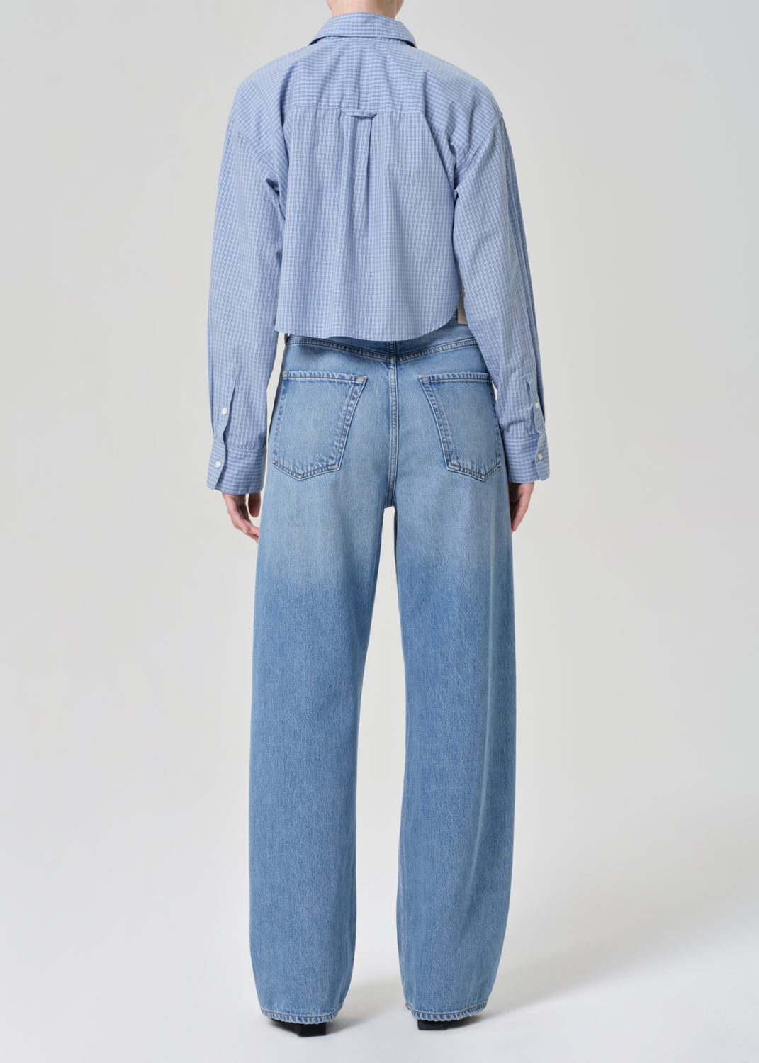 Person wearing a blue plaid shirt and jeans on a grey background