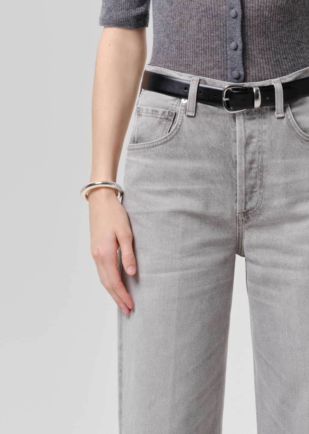 Person wearing a gray cardigan and light gray jeans on a grey background