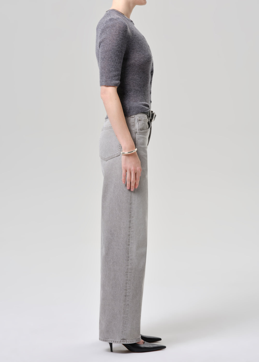 Person wearing a gray cardigan and light gray jeans on a grey background
