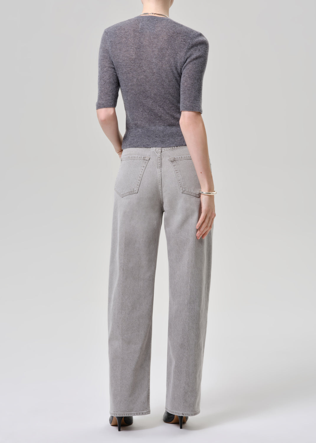 Person wearing a gray cardigan and light gray jeans on a grey background