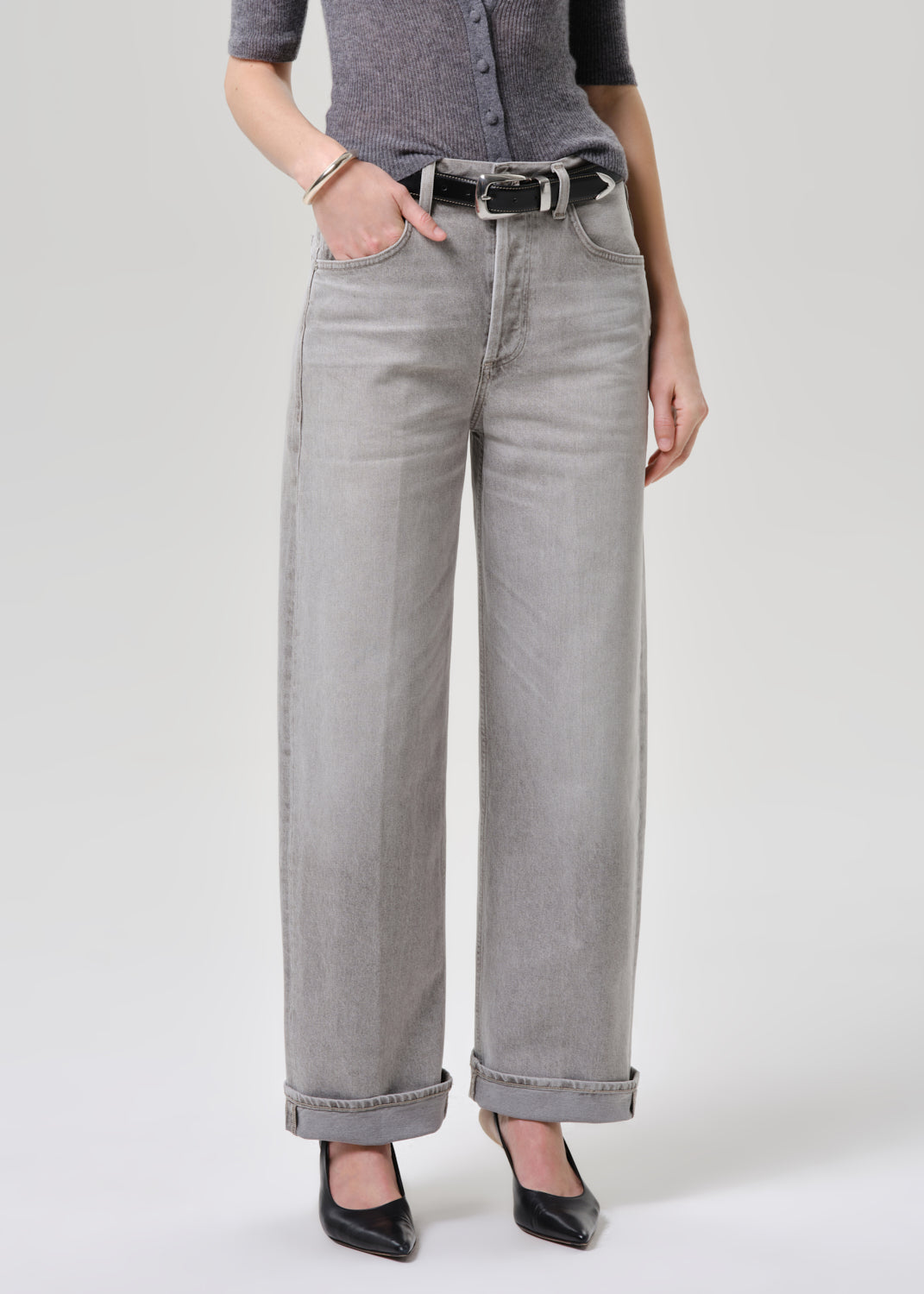 Person wearing a gray cardigan and light gray jeans on a grey background