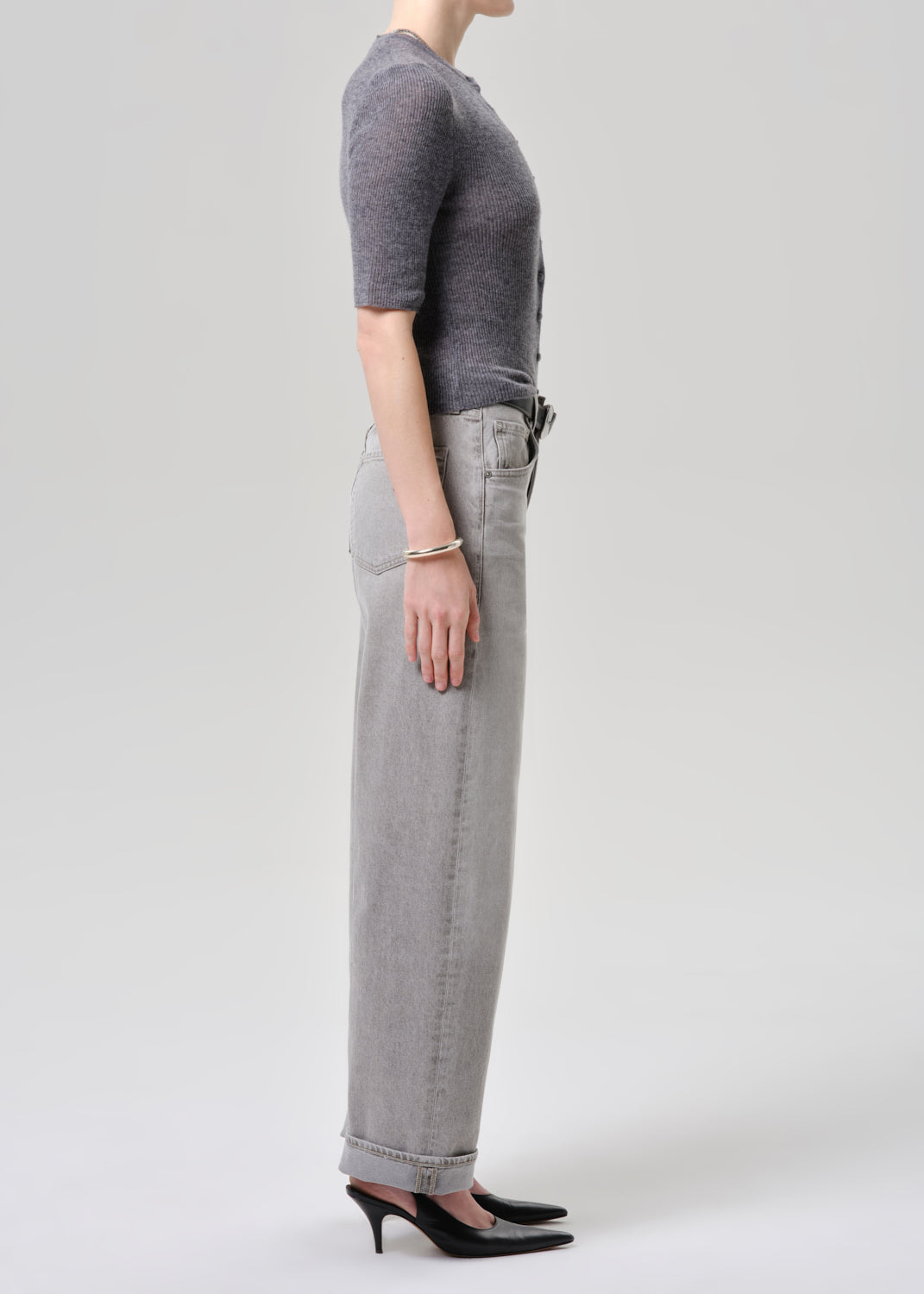 Person wearing a gray cardigan and light gray jeans on a grey background