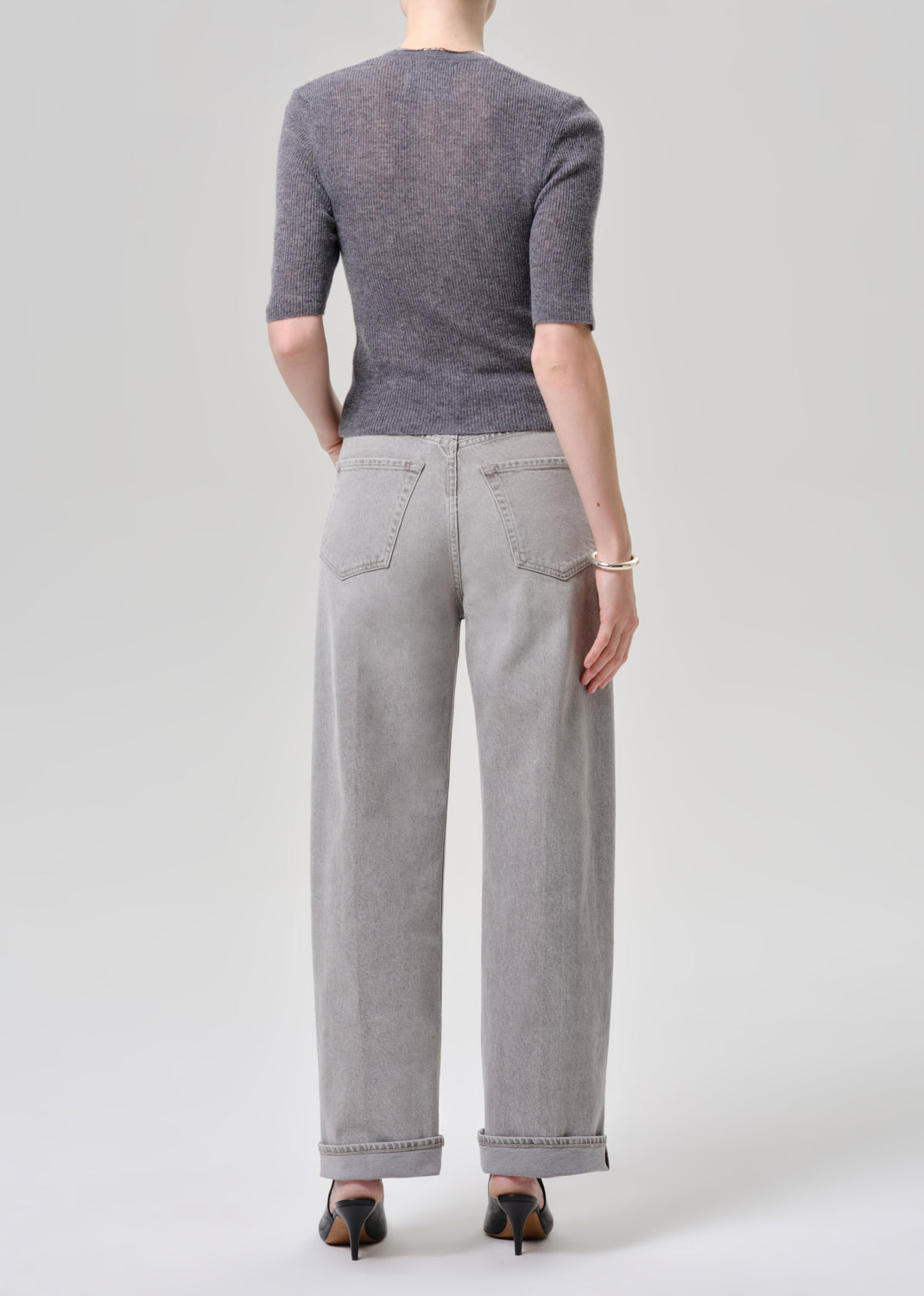 Person wearing a gray cardigan and light gray jeans on a grey background