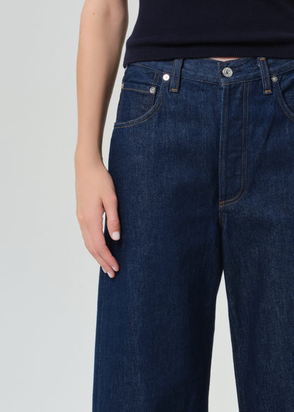 Person wearing a navy top and dark blue jeans on a grey  background