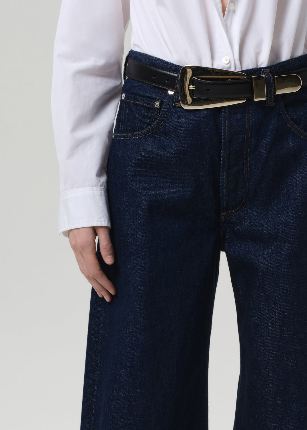 Person wearing dark blue jeans with a black belt on a plain background