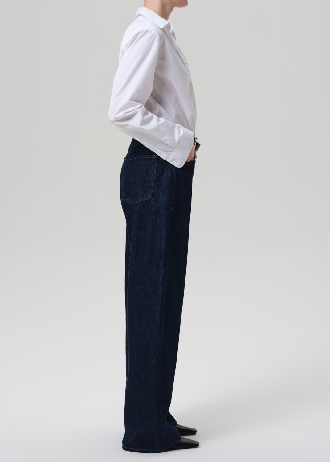 Person wearing a white shirt and dark blue jeans on a plain background