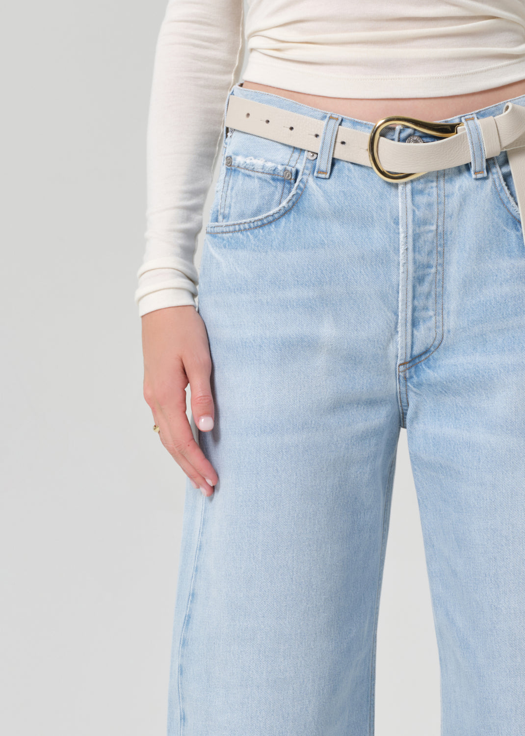 Person wearing light blue jeans and a cream long-sleeve top on a grey background