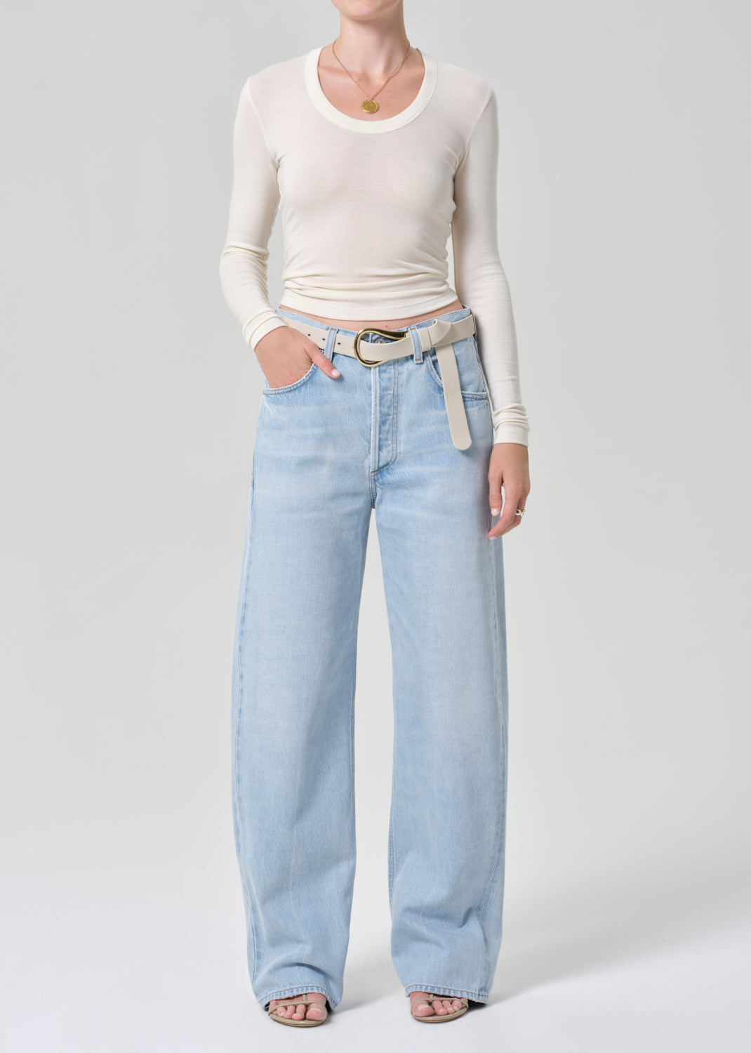 Person wearing light blue jeans and a cream long-sleeve top on a grey background