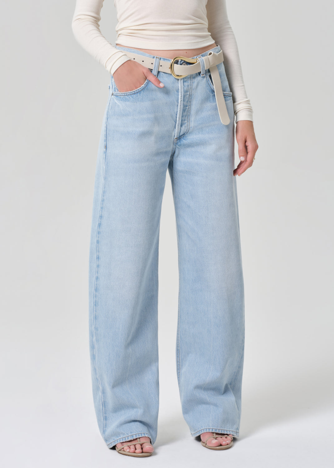 Person wearing light blue jeans and a cream long-sleeve top on a grey background