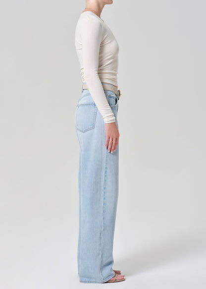 Person wearing light blue jeans and a cream long-sleeve top on a grey background