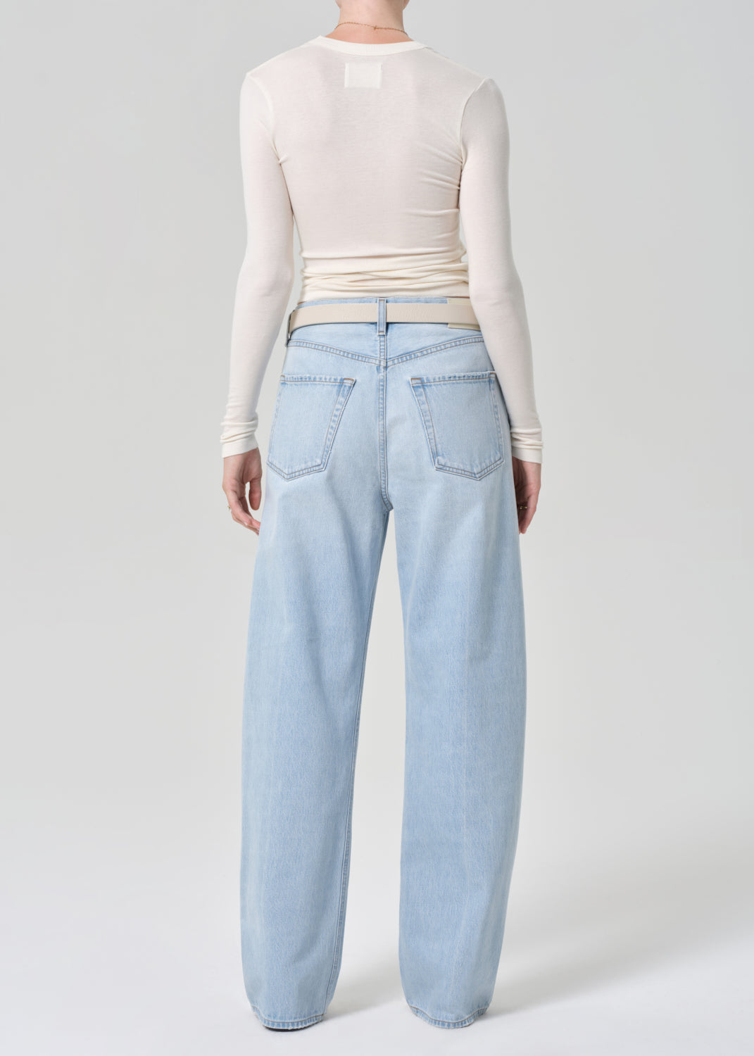 Person wearing light blue jeans and a cream long-sleeve top on a grey background