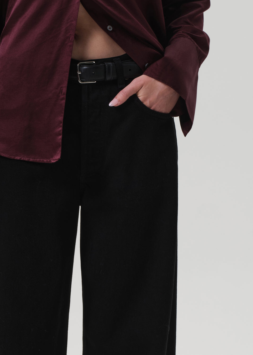 Person wearing a burgundy shirt and black pants on a plain background