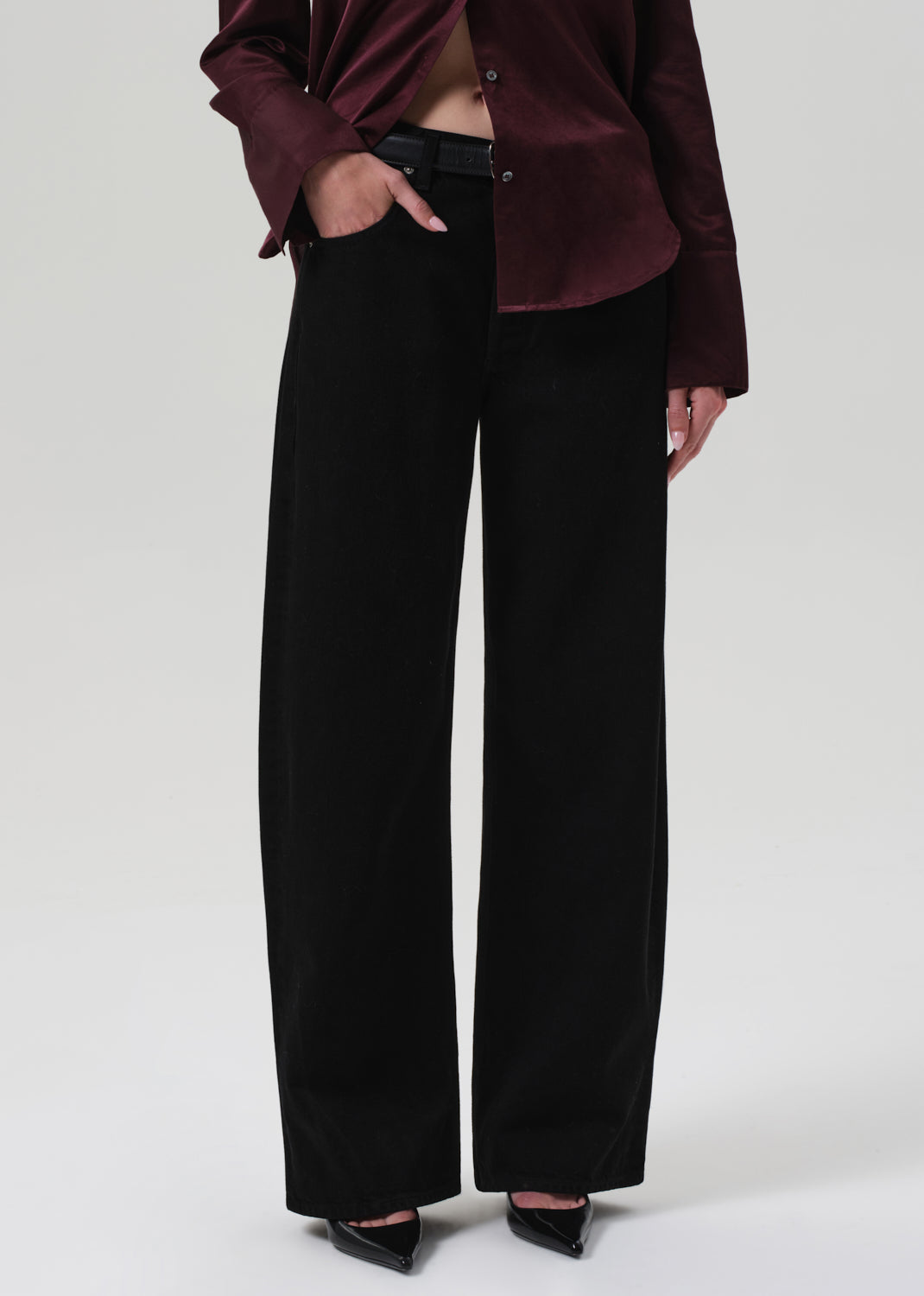 Person wearing a burgundy top and black pants on a white background