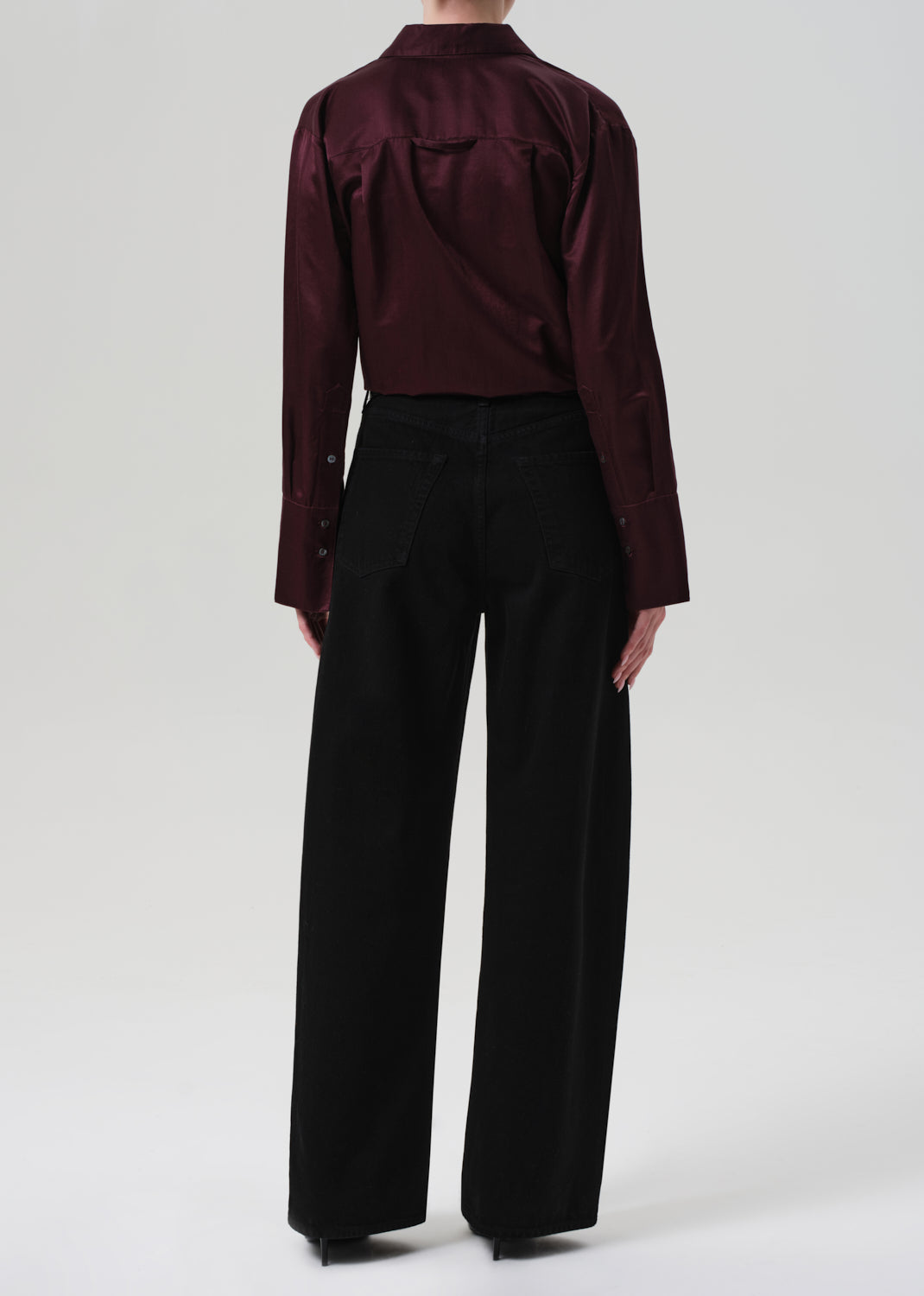 Person wearing a burgundy shirt and black pants on a white background
