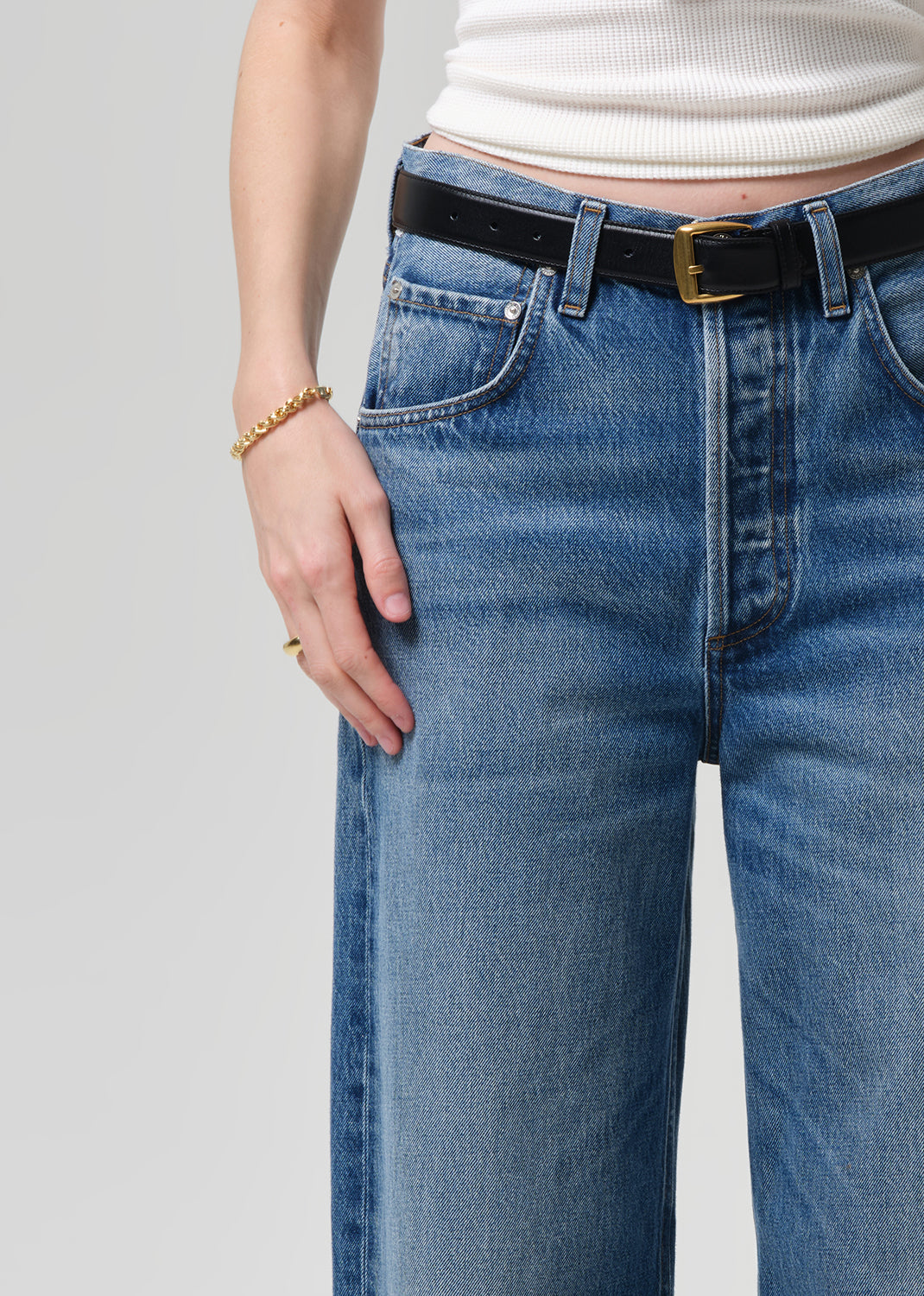 Person wearing blue jeans with a black belt on a plain background