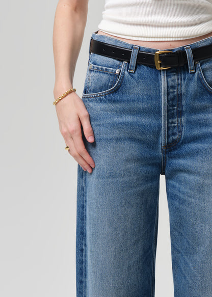 Person wearing blue jeans with a black belt on a plain background