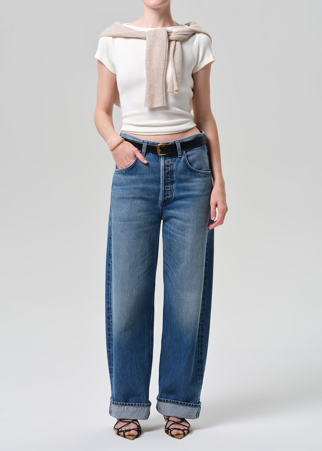 Person wearing a white top, beige scarf, and blue jeans on a plain background