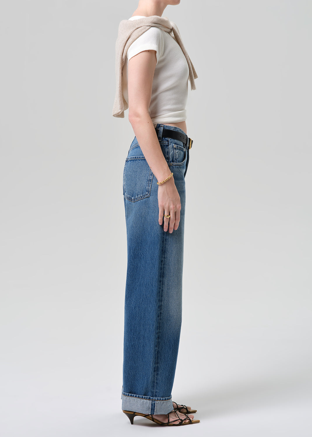 Person wearing blue jeans and a beige top on a plain background