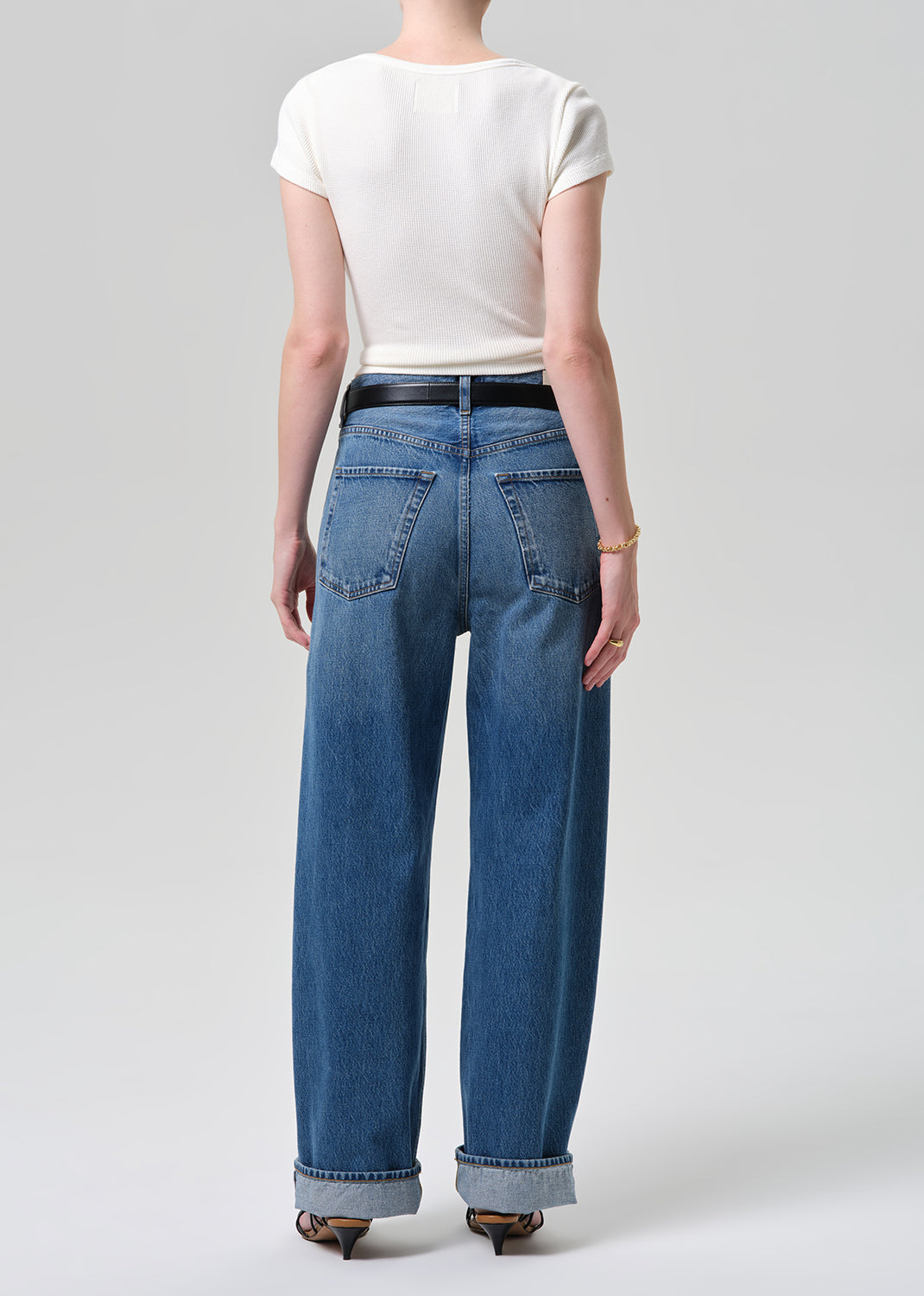 Person wearing blue jeans and a white top on a plain background