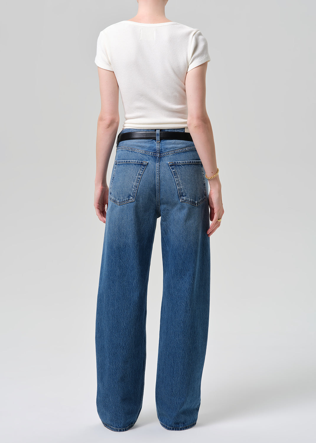 Person wearing blue jeans and a white top on a plain background