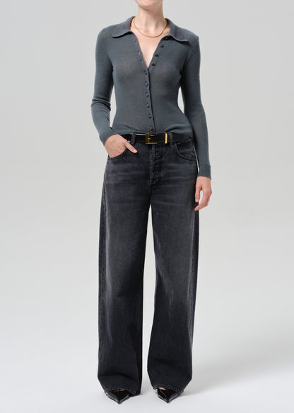 A model wearing a dark grey long-sleeve button-up knit top and wide-leg charcoal gray jeans with a gold-tone belt, photographed against a grey background.