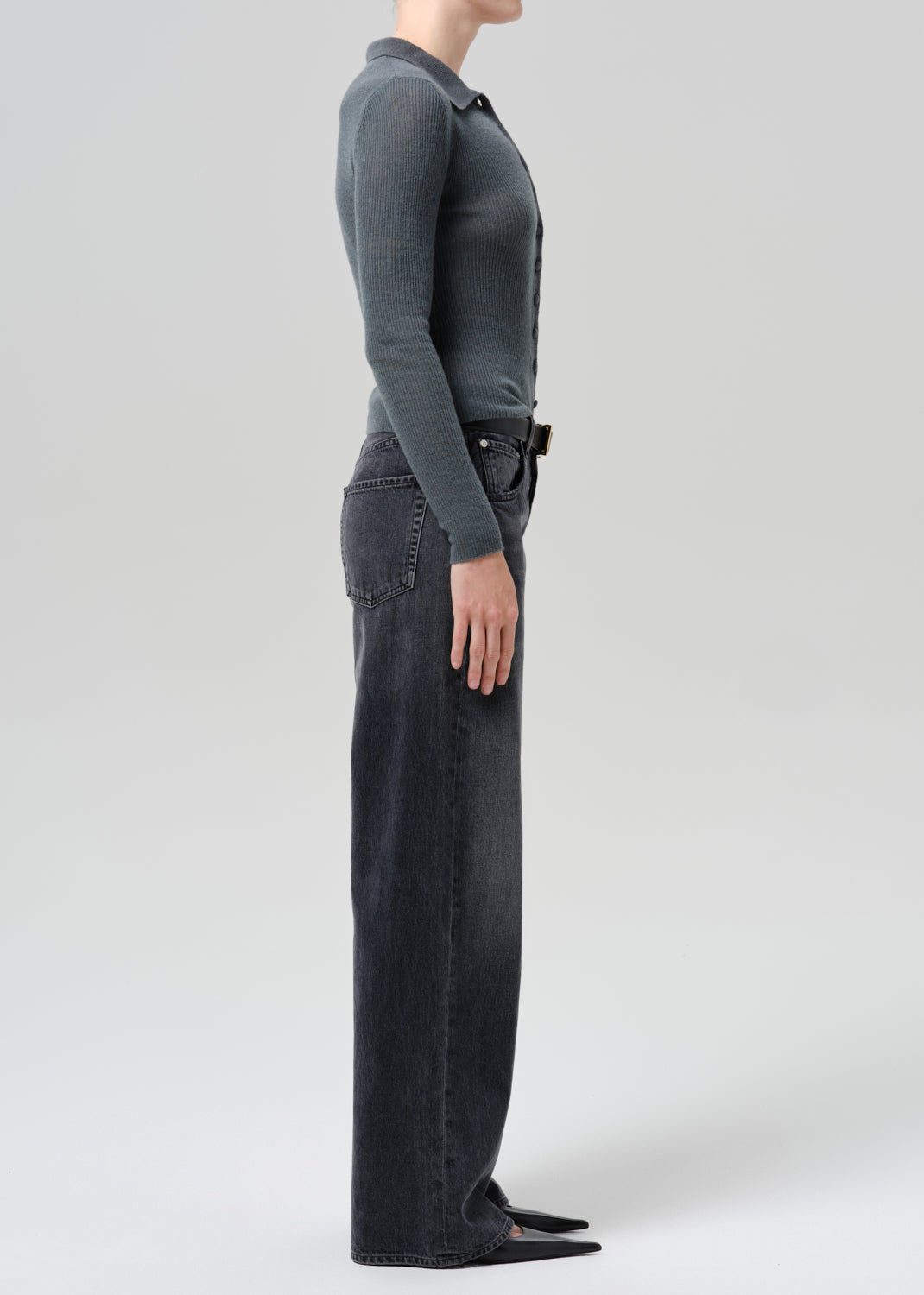 A model wearing a dark charcoal grey long-sleeve knit top and black wide-leg jeans against a grey background.