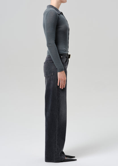 A model wearing a dark charcoal grey long-sleeve knit top and black wide-leg jeans against a grey background.