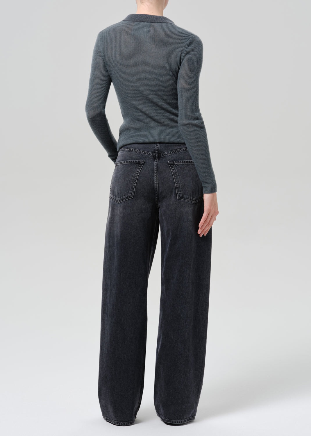 A model wearing a dark charcoal grey long-sleeve knit top and black wide-leg jeans against a grey background.