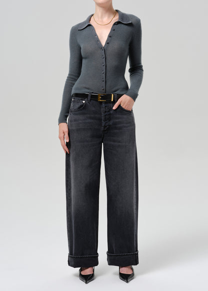A model wearing a dark gray long-sleeve button-up knit top and black wide-leg jeans with a black belt, standing against a grey background.