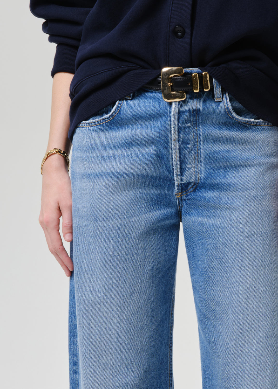 Close-up of blue jeans with a gold belt on a grey background