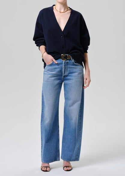 Person wearing a navy cardigan and blue jeans on a grey background