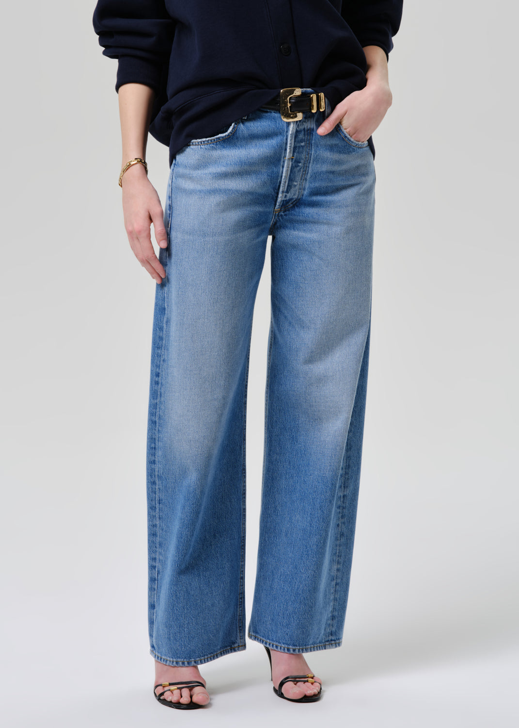 Person wearing blue jeans and a dark top on a grey background